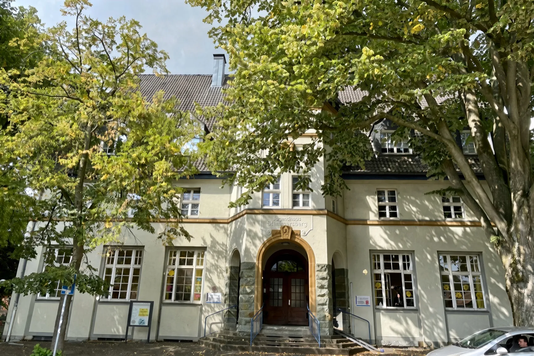 Das ehemalige Jugendhaus heute: hell verputztes Gebäude mit Rundbogenportal zwischen Bäumen.